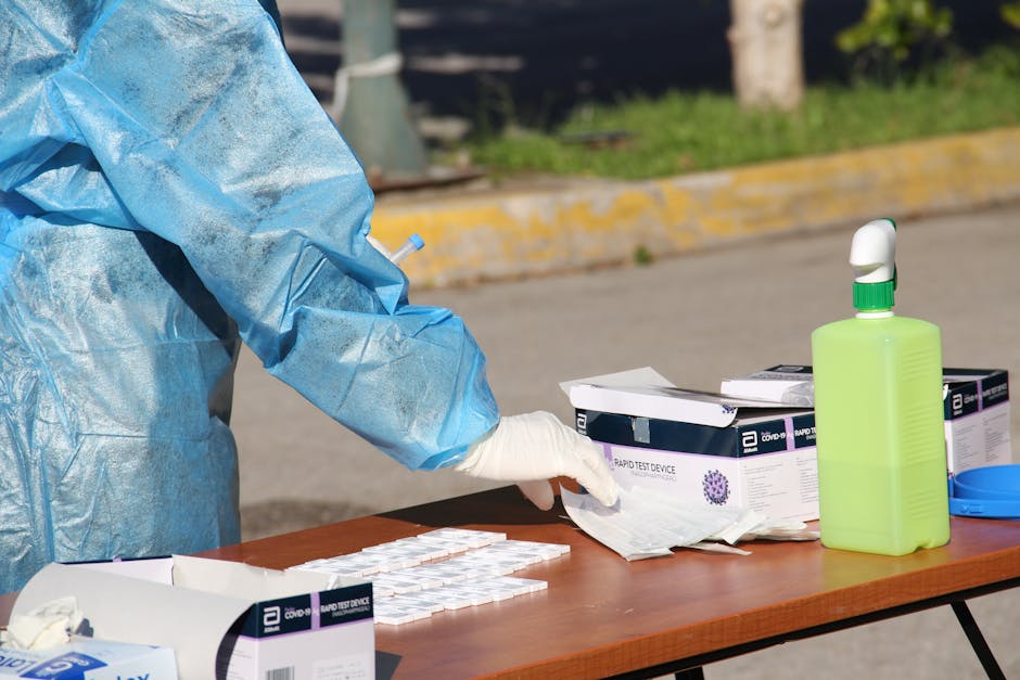 Healthcare worker in protective gear conducting rapid COVID-19 testing outdoors. PPE and test kits visible.