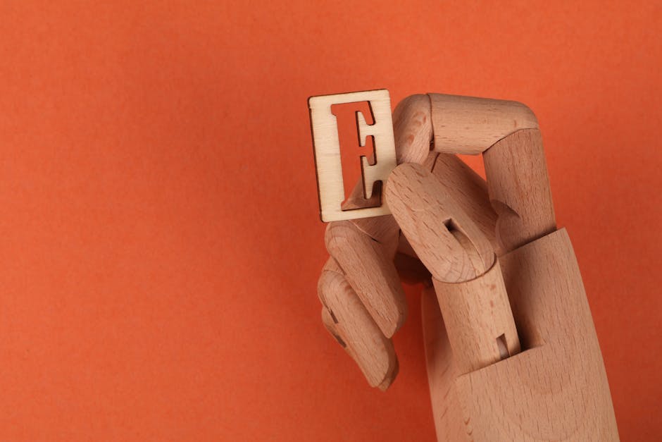 A wooden mannequin hand holding a wooden letter 'E' on an orange background.