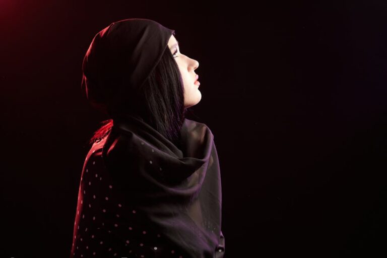Side profile of a woman wearing a black polka dot headscarf, illuminated by dramatic side lighting.