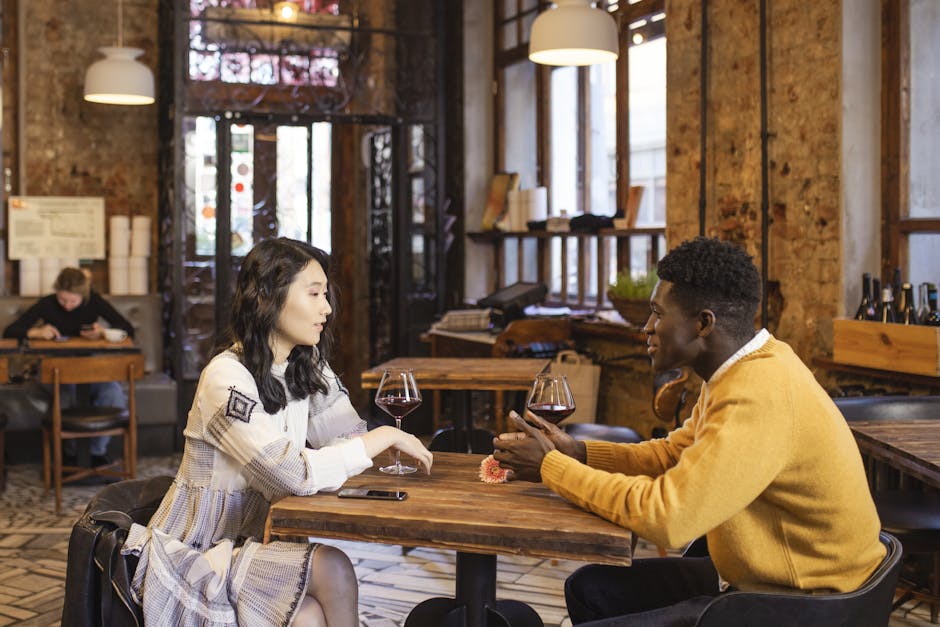 An Asian woman and Black man enjoy a romantic date with wine in a stylish café.