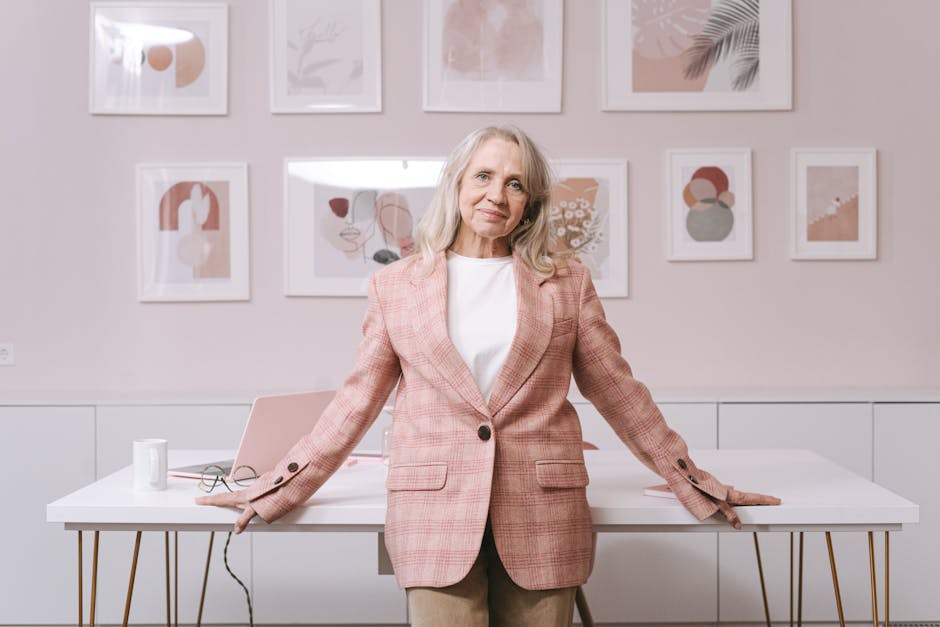 Elderly woman in pink blazer confidently posing in a stylish home office environment.