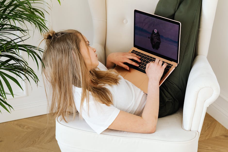 Teen girl comfortably lounging in armchair, browsing a laptop at home.
