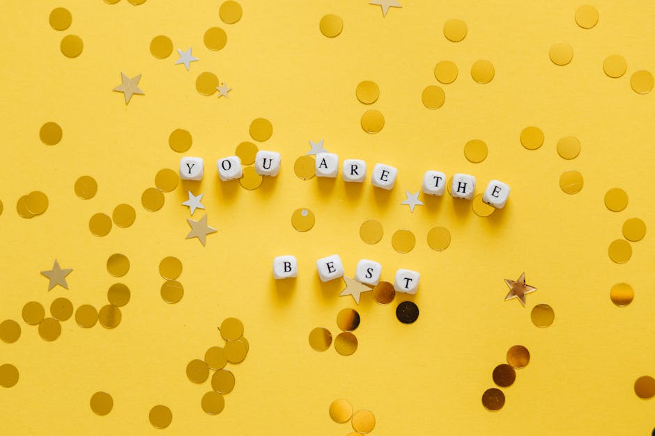 Inspirational message ‘You Are the Best’ spelled with dice on a vibrant yellow surface with star confetti.