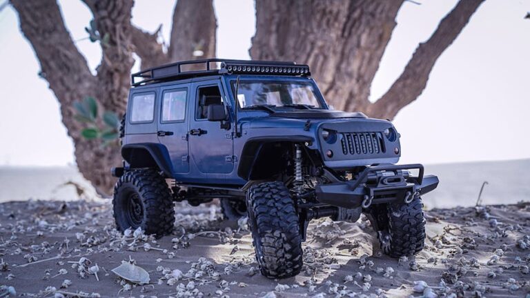Miniature off-road toy car parked on sandy ground with tree backdrop, captured outdoors in daylight.