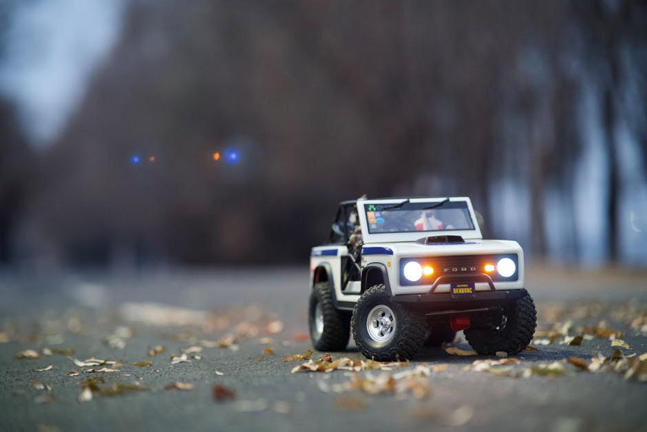 Miniature off-road toy car on a street with scattered leaves, headlights on.