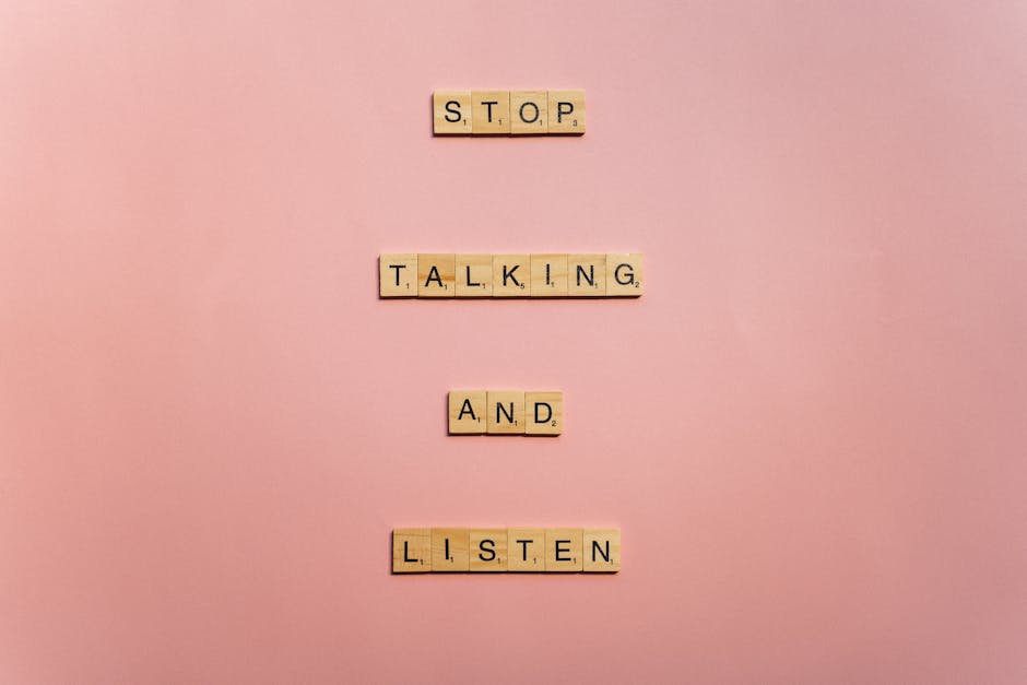 Wooden scrabble tiles form the message 'Stop talking and listen' on a pink surface.