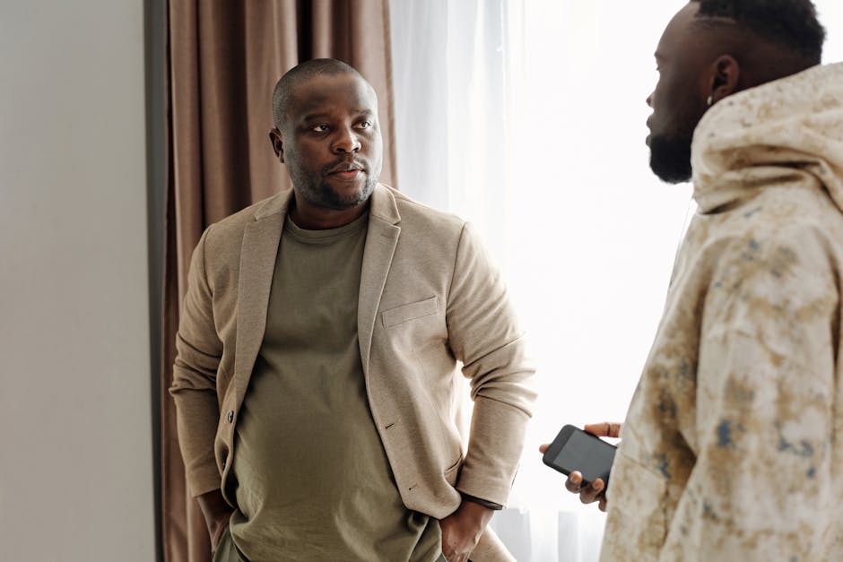 Two men engaged in a serious conversation indoors, one holding a smartphone.