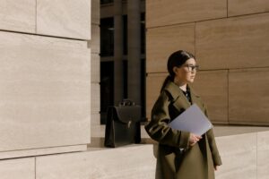 Asian businesswoman in a coat holding a folder by modern building, daytime.