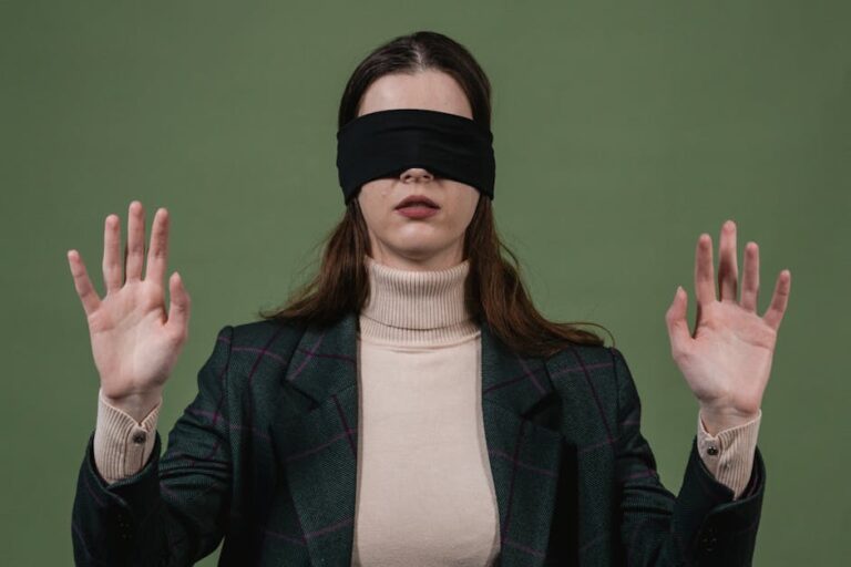 Blindfolded woman standing with hands raised against a green background.