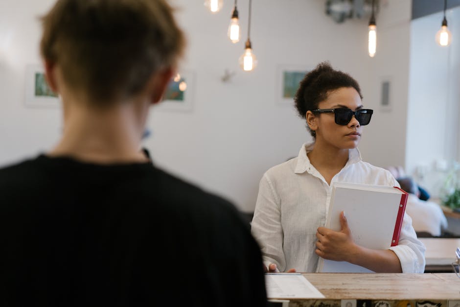 A woman with visual impairment holding a book, standing in a cafe.
