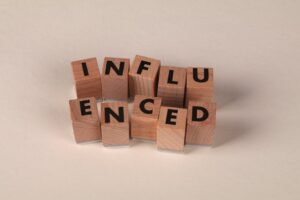 Wooden letter blocks arranged to spell 'Influenced' on a neutral beige surface.