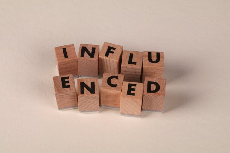 Wooden letter blocks arranged to spell 'Influenced' on a neutral beige surface.