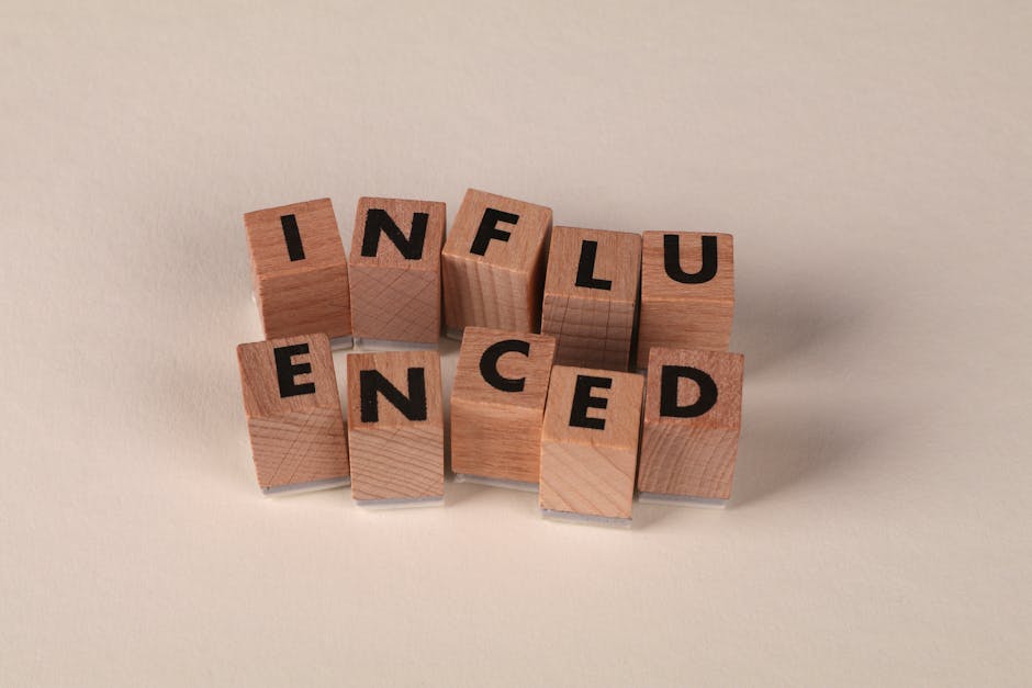Wooden letter blocks arranged to spell 'Influenced' on a neutral beige surface.