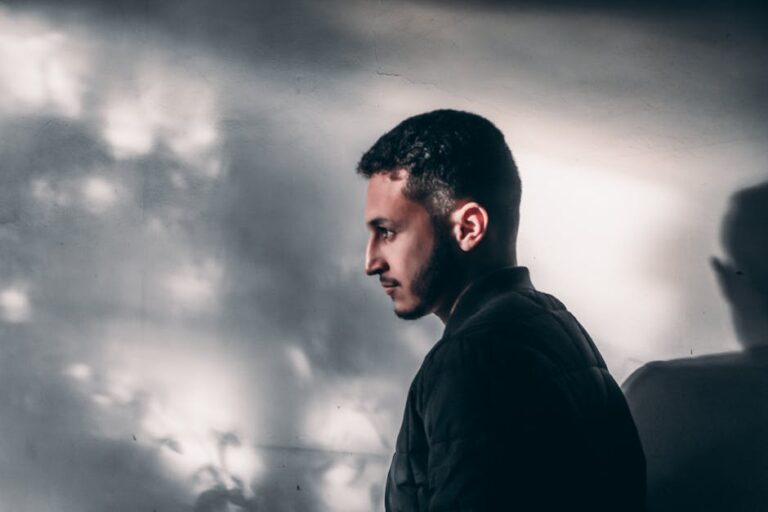 Side profile of a contemplative man with shadows on the wall, exuding a moody vibe.