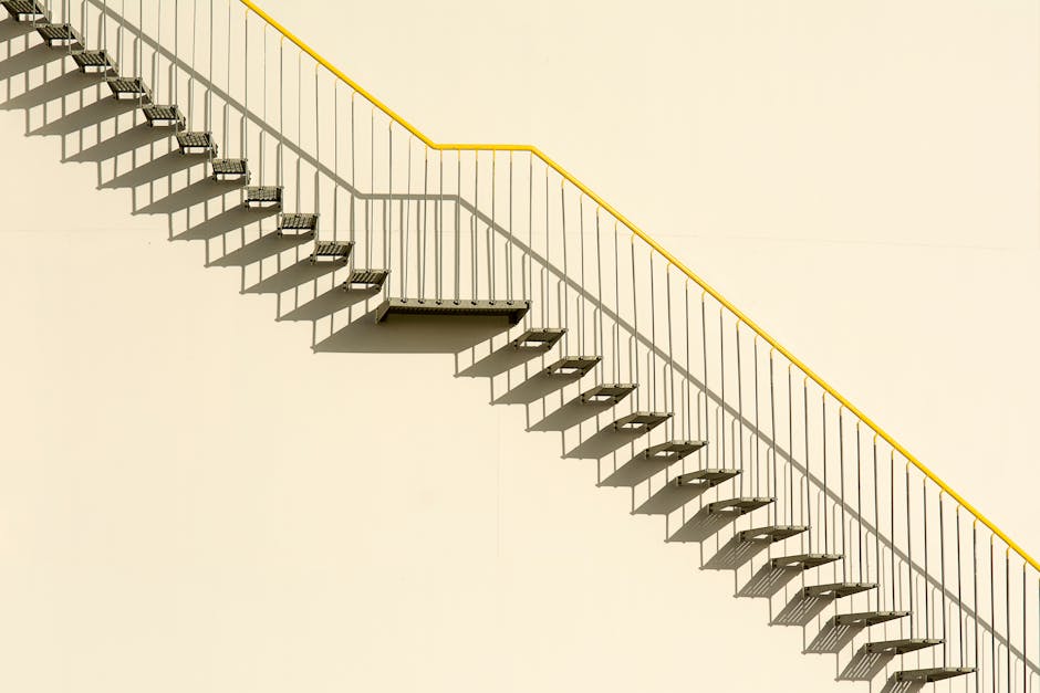 A simple outdoor metal staircase on a concrete wall casting shadows, showcasing minimalistic architecture.