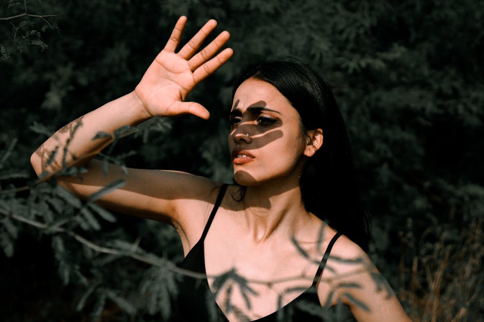 A striking portrait of a woman with dramatic shadows across her face and background foliage.