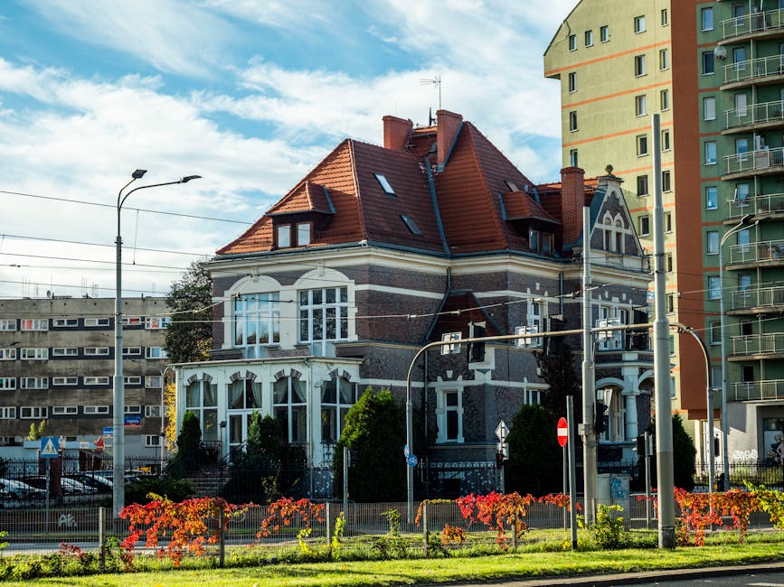 Beautiful old house with red roof surrounded by modern city buildings.