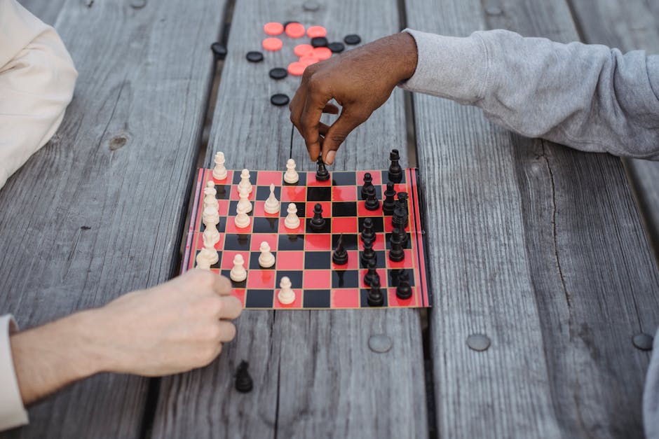 From above of crop anonymous multiethnic friends playing chess sitting at wooden table