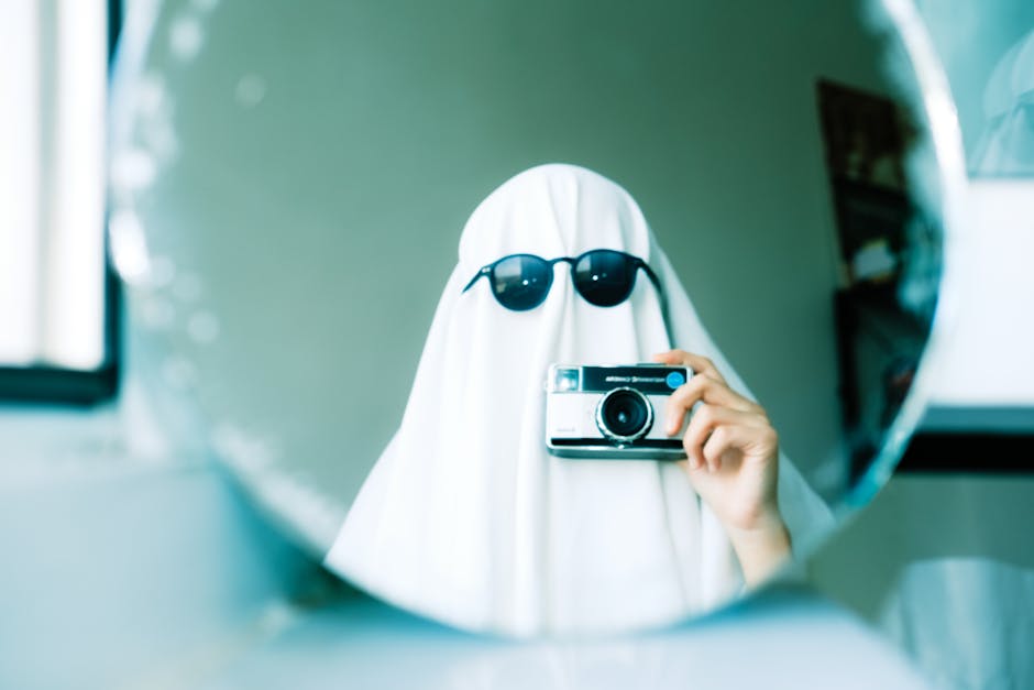 Imaginative Halloween ghost costume using a sheet and sunglasses, holding a camera in front of a mirror.