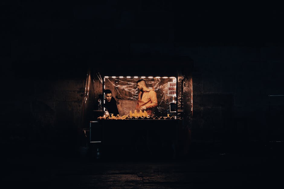 A dimly lit market stall selling fruits by two people at night, creating a moody atmosphere.