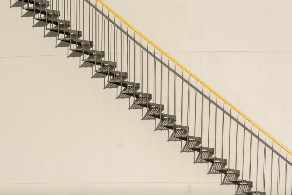 A modern outdoor metal staircase casting shadows on a white wall under bright sunlight.