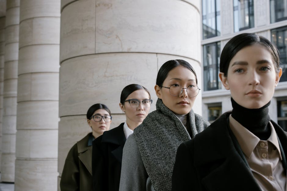 Four diverse women in business attire stand confidently in an urban setting, showcasing modern elegance.
