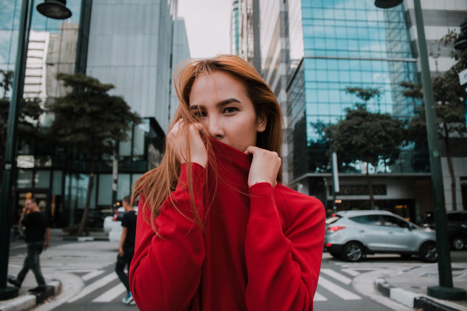 Stylish woman in red sweater posing in bustling city street with modern architecture.