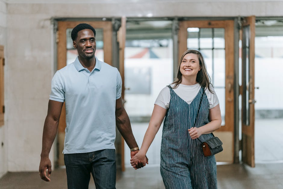 Smiling multiracial couple holding hands in an indoor setting, showcasing happiness and connection.