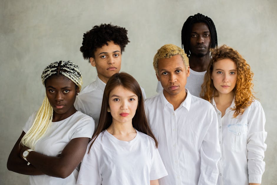 Serious diverse multiracial people standing close together representing concept of unity and looking at camera against gray