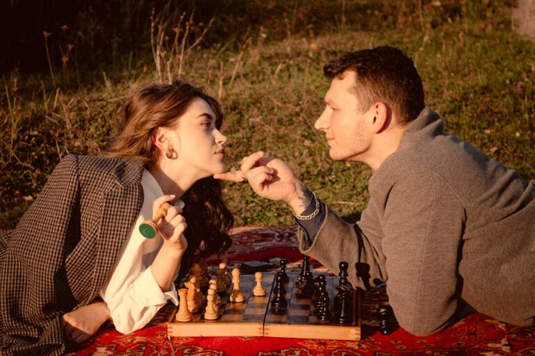 A couple lying on a blanket playing chess in a sunny outdoor setting.