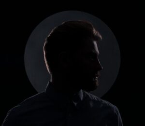 Moody silhouette profile of a man against a dark background with a circular spotlight.