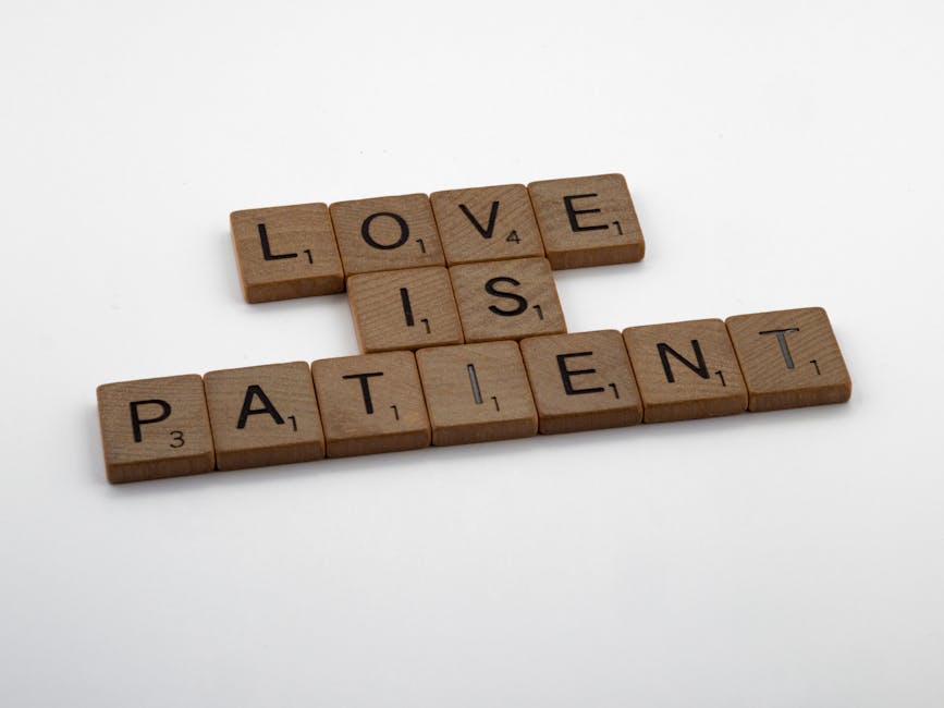 Scrabble tiles displaying the words 'Love is Patient' on a plain background.