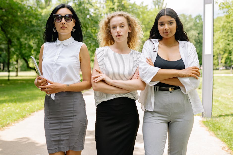 Three confident businesswomen stand with arms crossed in an outdoor park setting, exuding professionalism.