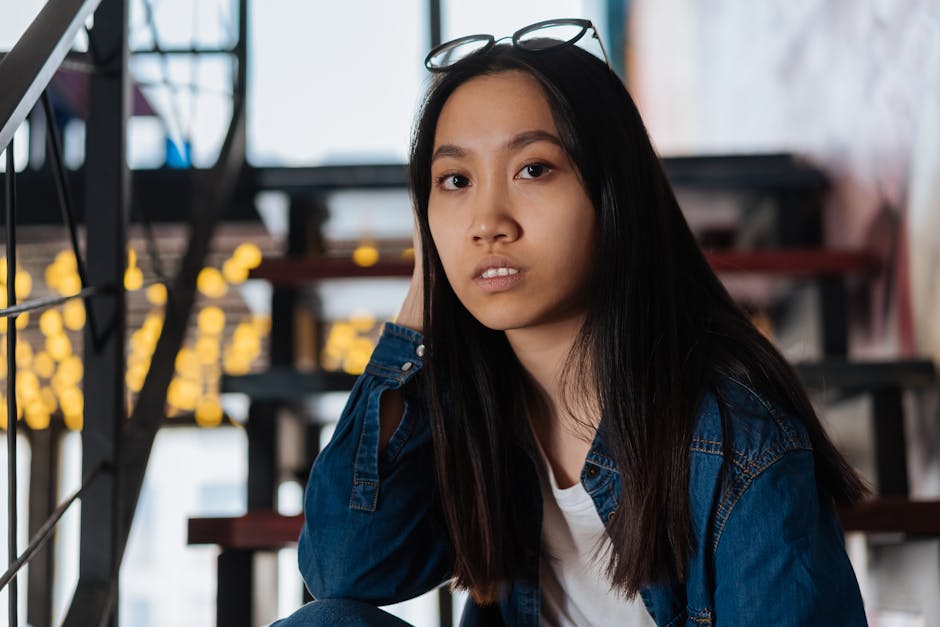 Close-up portrait of a young woman in eyeglasses and denim jacket indoors.