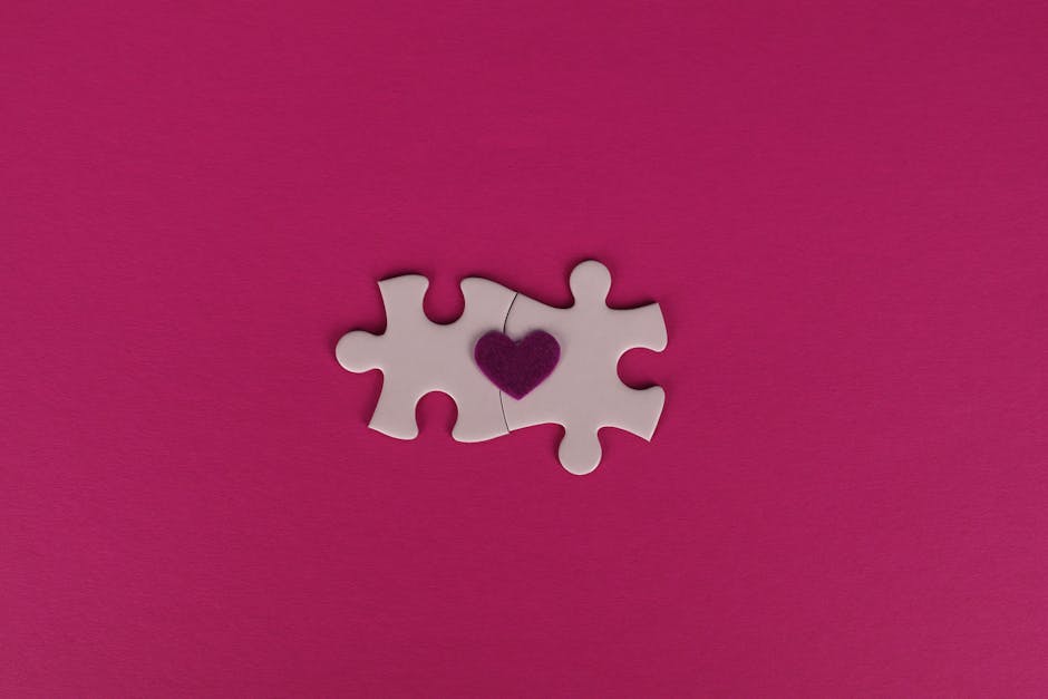 Two white puzzle pieces with a heart symbol on a pink background, symbolizing love and connection.