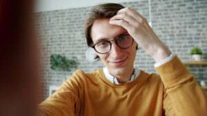 Casual portrait of a young man with glasses and yellow sweater indoors.