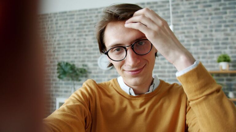 Casual portrait of a young man with glasses and yellow sweater indoors.