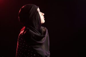 Side profile of a woman wearing a black polka dot headscarf, illuminated by dramatic side lighting.