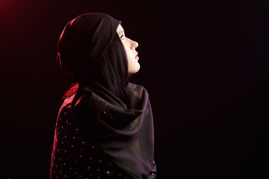 Side profile of a woman wearing a black polka dot headscarf, illuminated by dramatic side lighting.