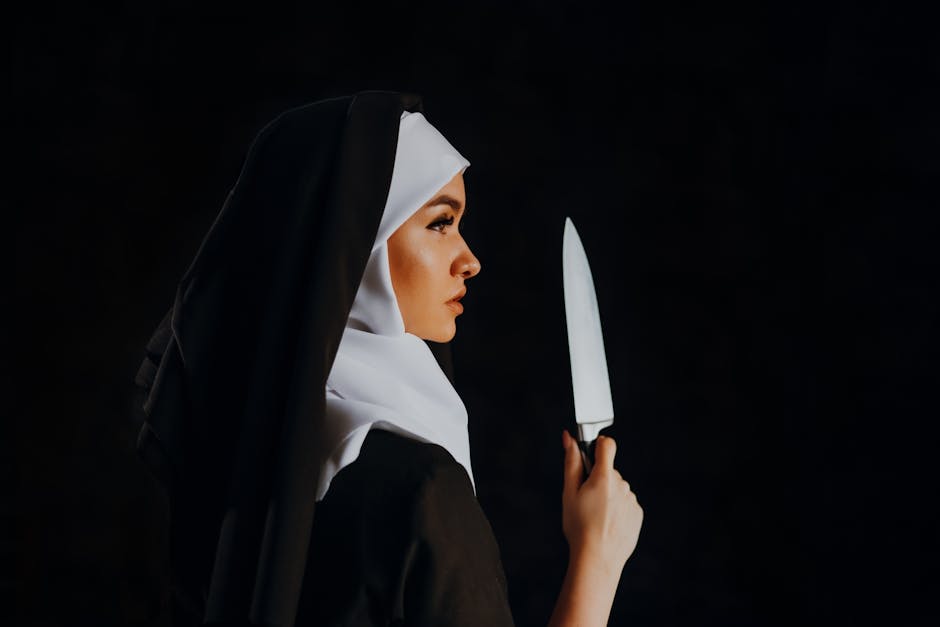 Side view of a nun holding a knife against a black background, creating a mysterious and intriguing scene.