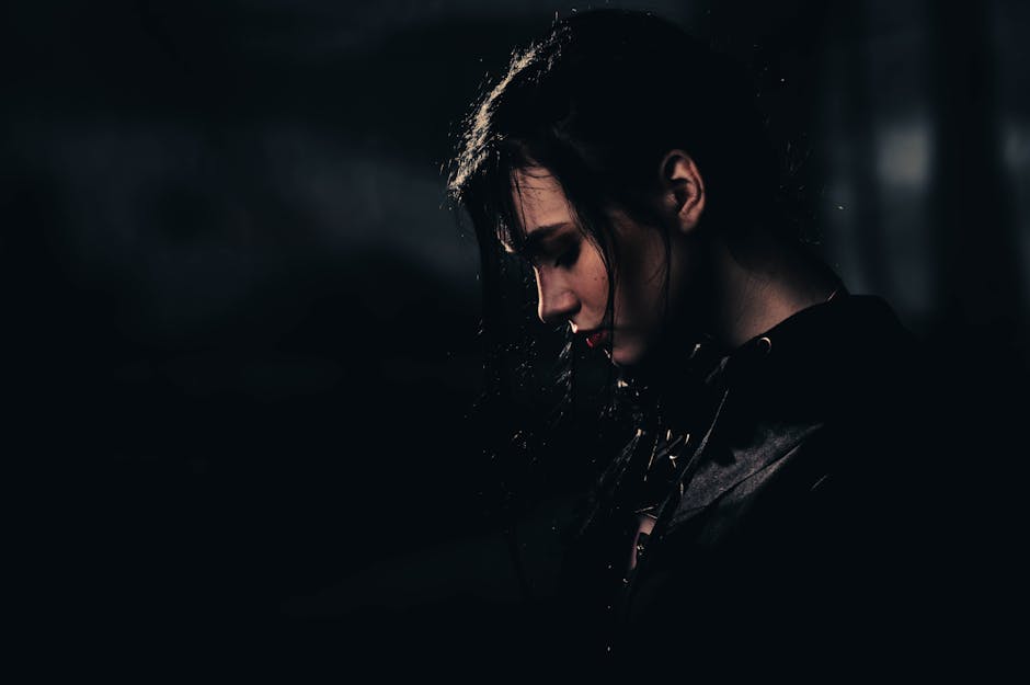 A dramatic portrait of a woman with black hair in a dark setting, evoking mystery and contemplation.