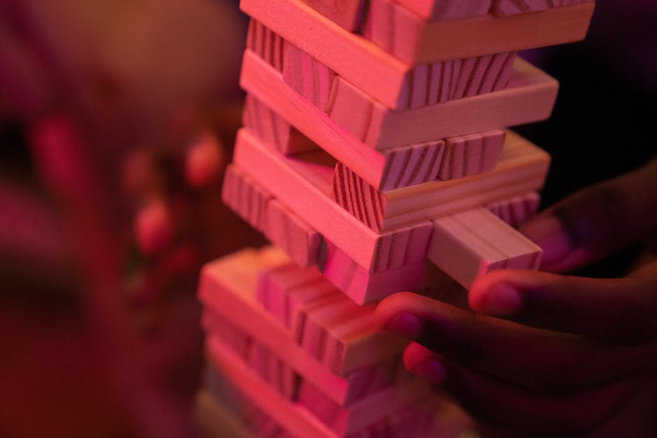 Close-up of hands playing a wooden block stacking game with pink lighting, capturing concentration and balance.