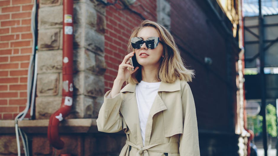 Fashionable woman in sunglasses using smartphone outdoors.