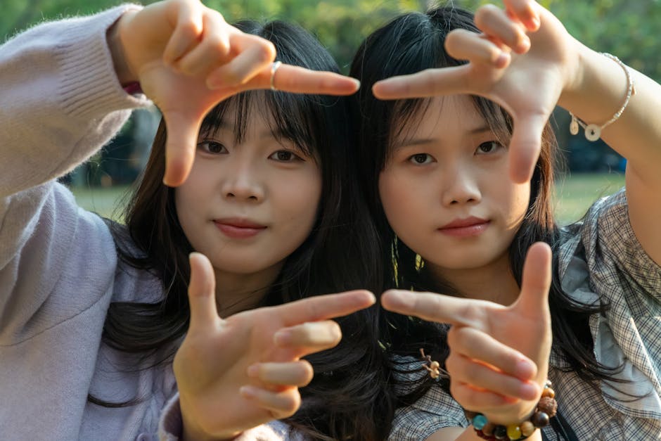 A close-up outdoor portrait of two young women using their hands to create a frame, capturing a creative and playful moment.