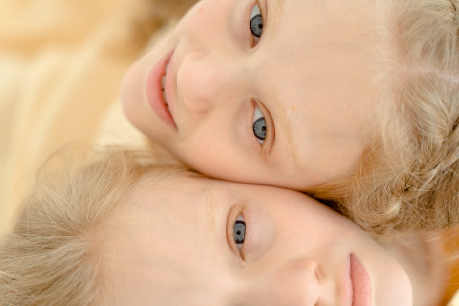 Delightful portrait of twin girls with blond hair, close-up view highlighting their joyful expressions and togetherness.