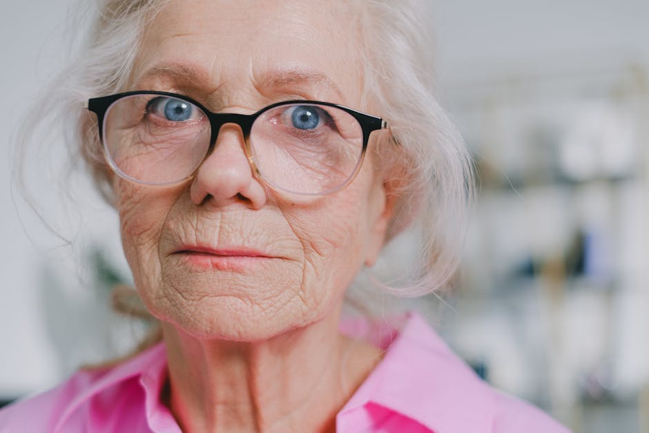 Elderly woman wearing glasses, looking thoughtful in a close-up portrait.