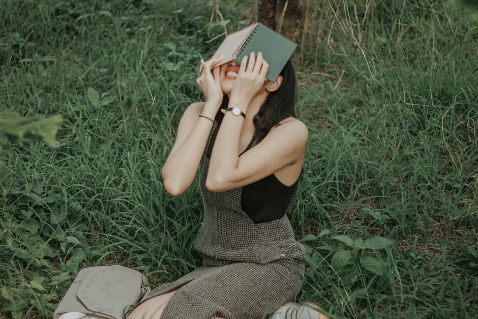 A young woman enjoying a sunny day outdoors, sitting in the grass with a book.