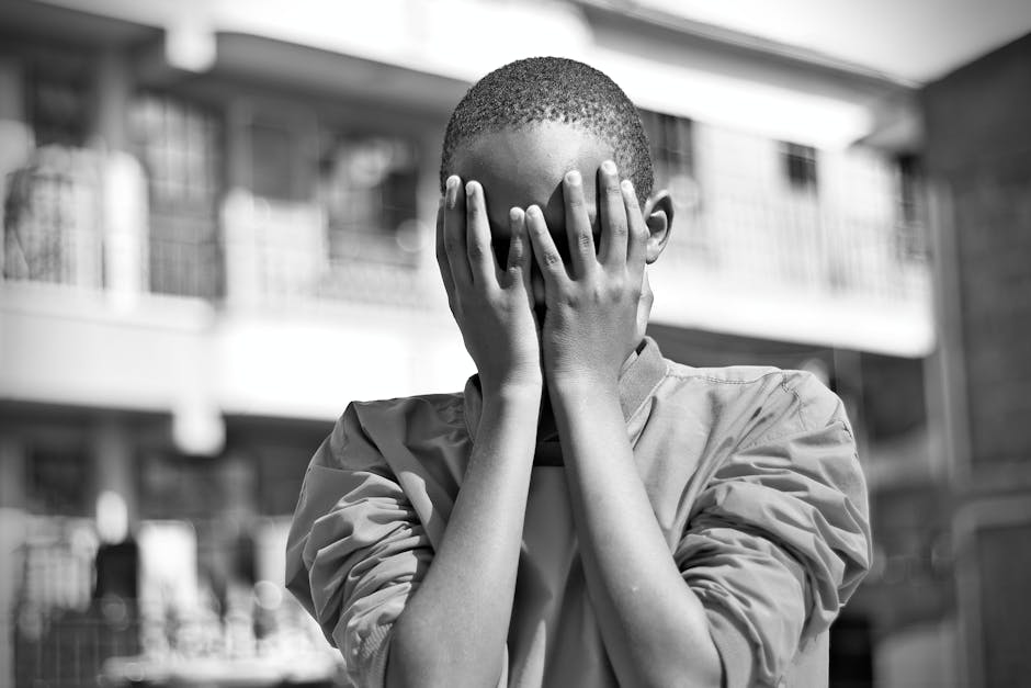 Black and white image of a child covering their face with hands outdoors in Nairobi.
