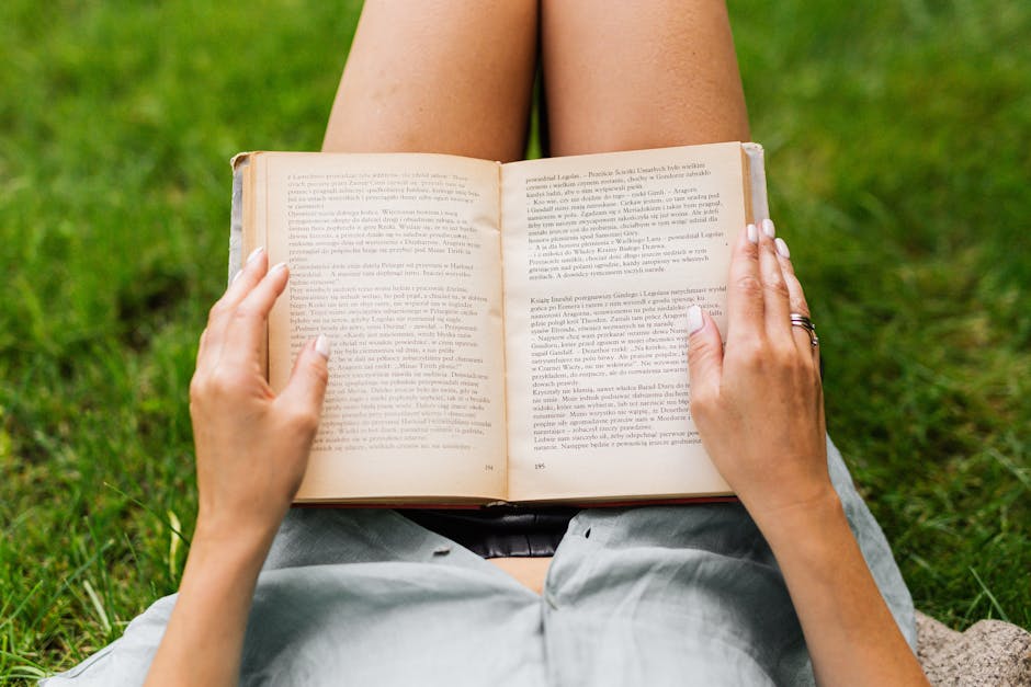 Woman enjoying a peaceful time reading a book outdoors on a grassy lawn.