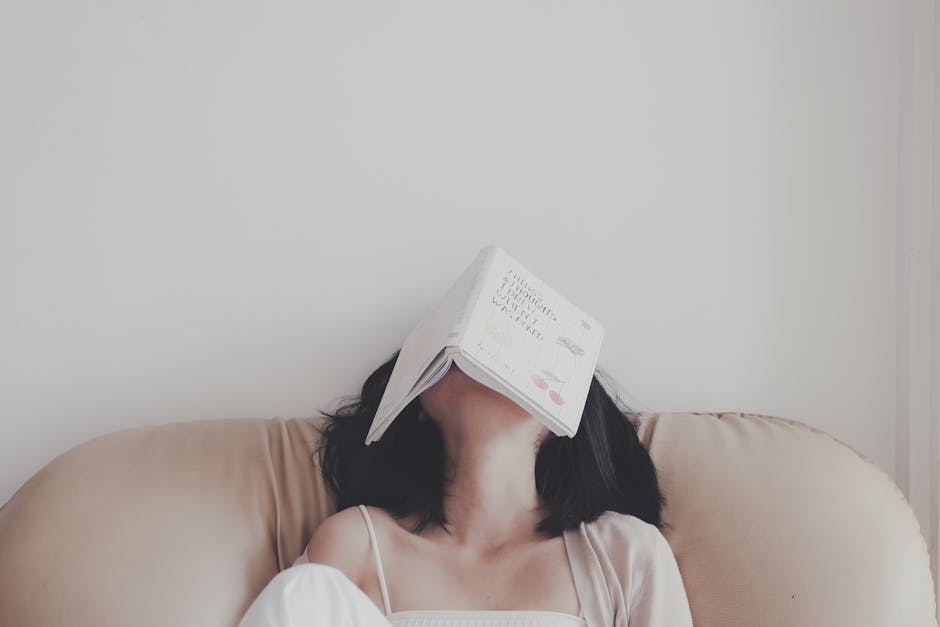 A woman relaxes indoors with an open book resting on her face, enjoying a tranquil moment.